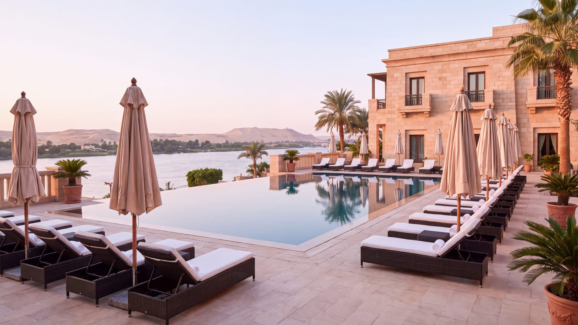 A hotel pool terrace at dawn, loungers aligned along still water.