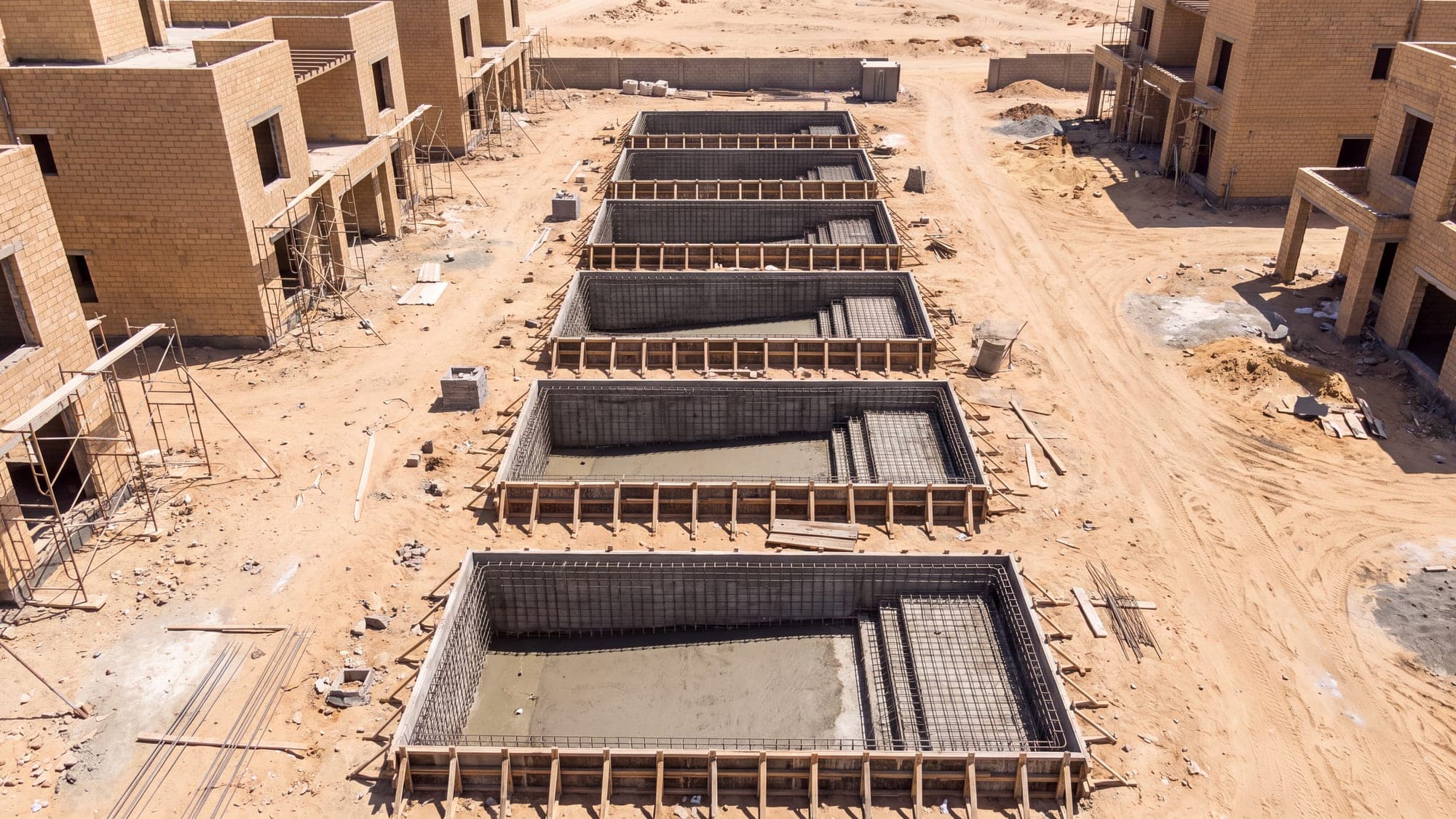 Identical villa pool shells in a row at the same construction stage.