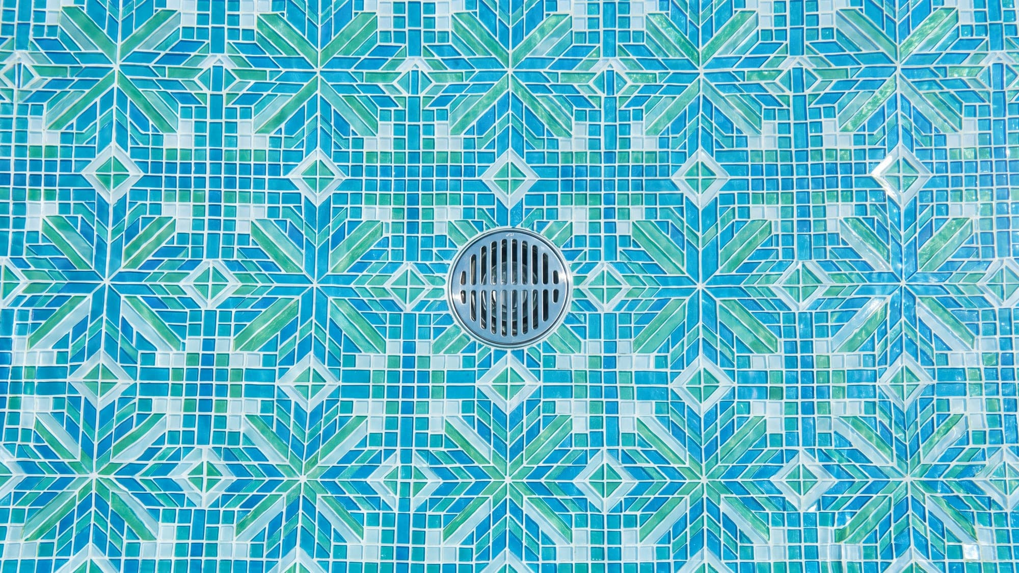 Crystal-clear pool water over a pristine mosaic floor, seen from above.